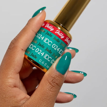 Manicured hand holding the DC Jelly 024 Jade jelly nail polish bottle, showcasing the turquoise green blue color on the nails