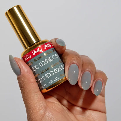 Manicured hand holding the DC Jelly 025 Storm jelly nail polish bottle, showcasing the warm grey color on the nails