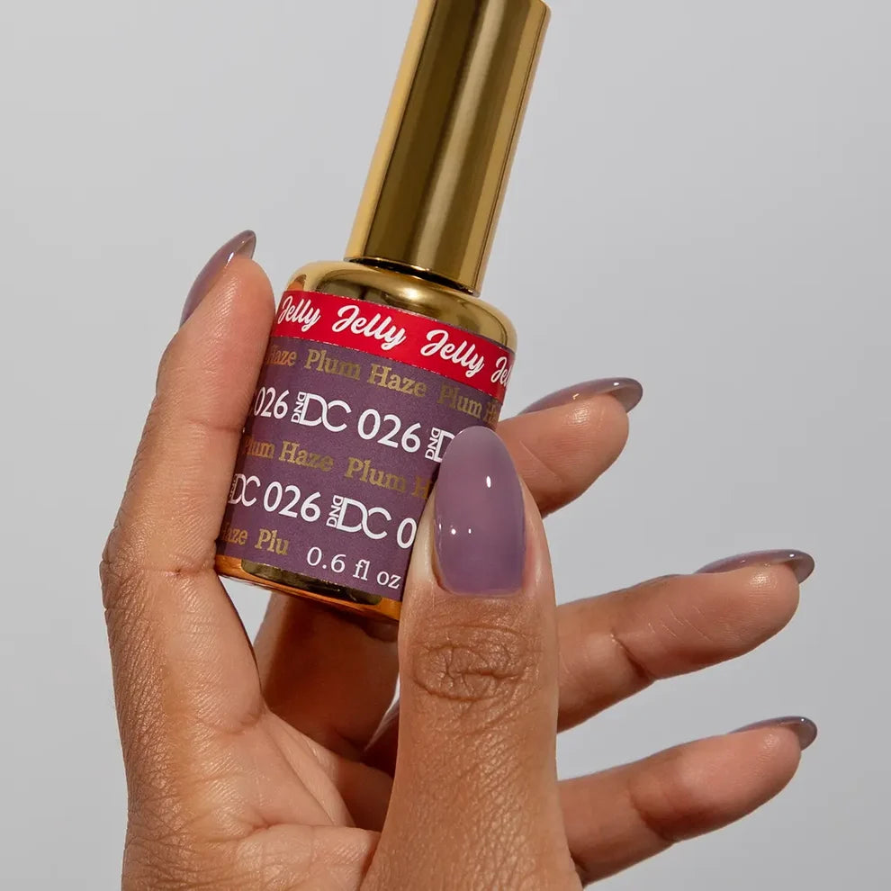 Manicured hand holding the DC Jelly 026 Plum Haze jelly nail polish bottle, showcasing the muted plum purple color on the nails