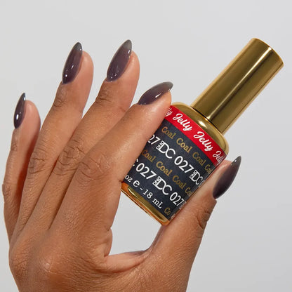 Manicured hand holding the jelly nail polish bottle for DC Jelly 027 Coal, showcasing the smoky dark grey color on the nails