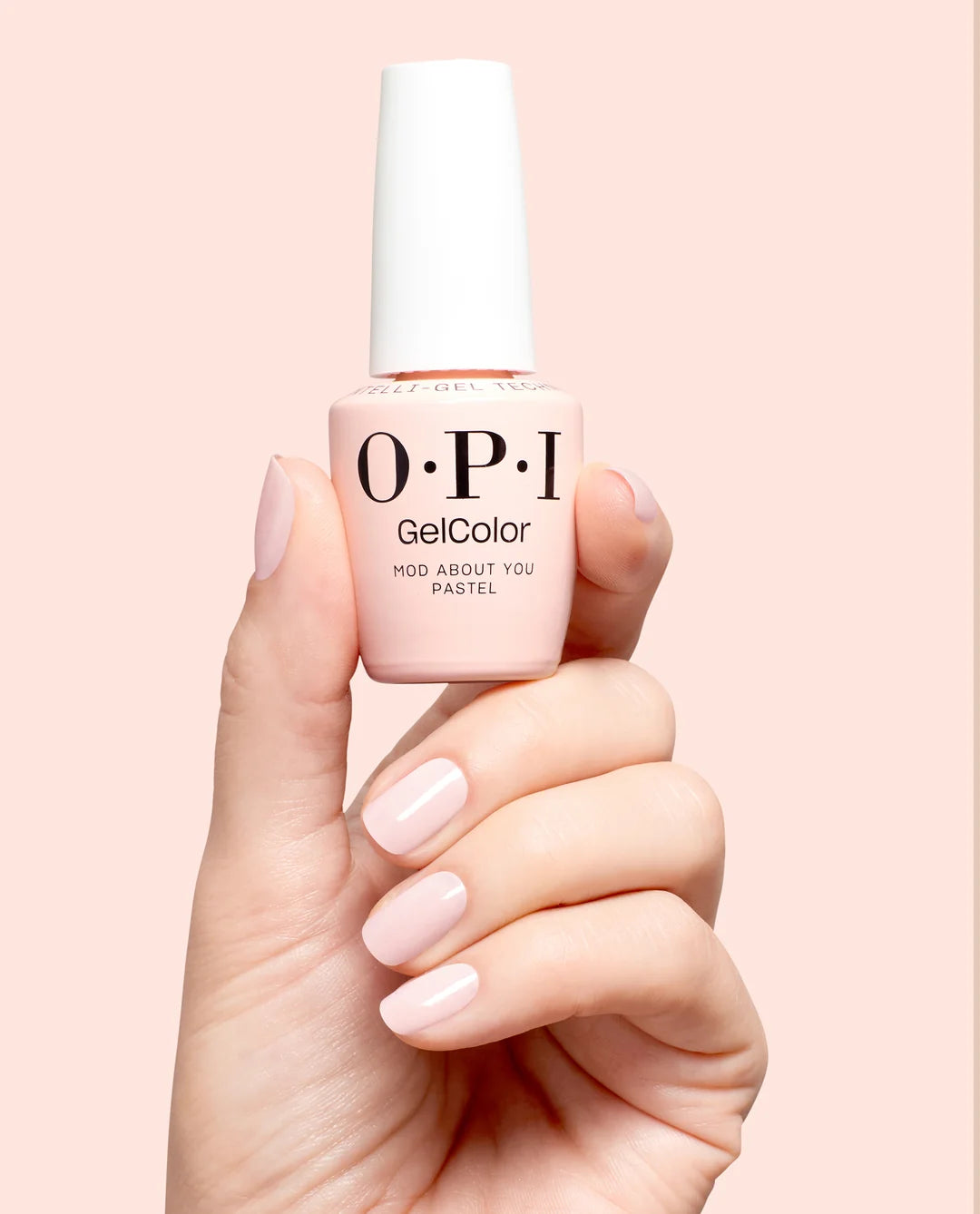 Hand holding a bottle of OPI GelColor mod about you pastel gel polish with a light pink shade on a matching background