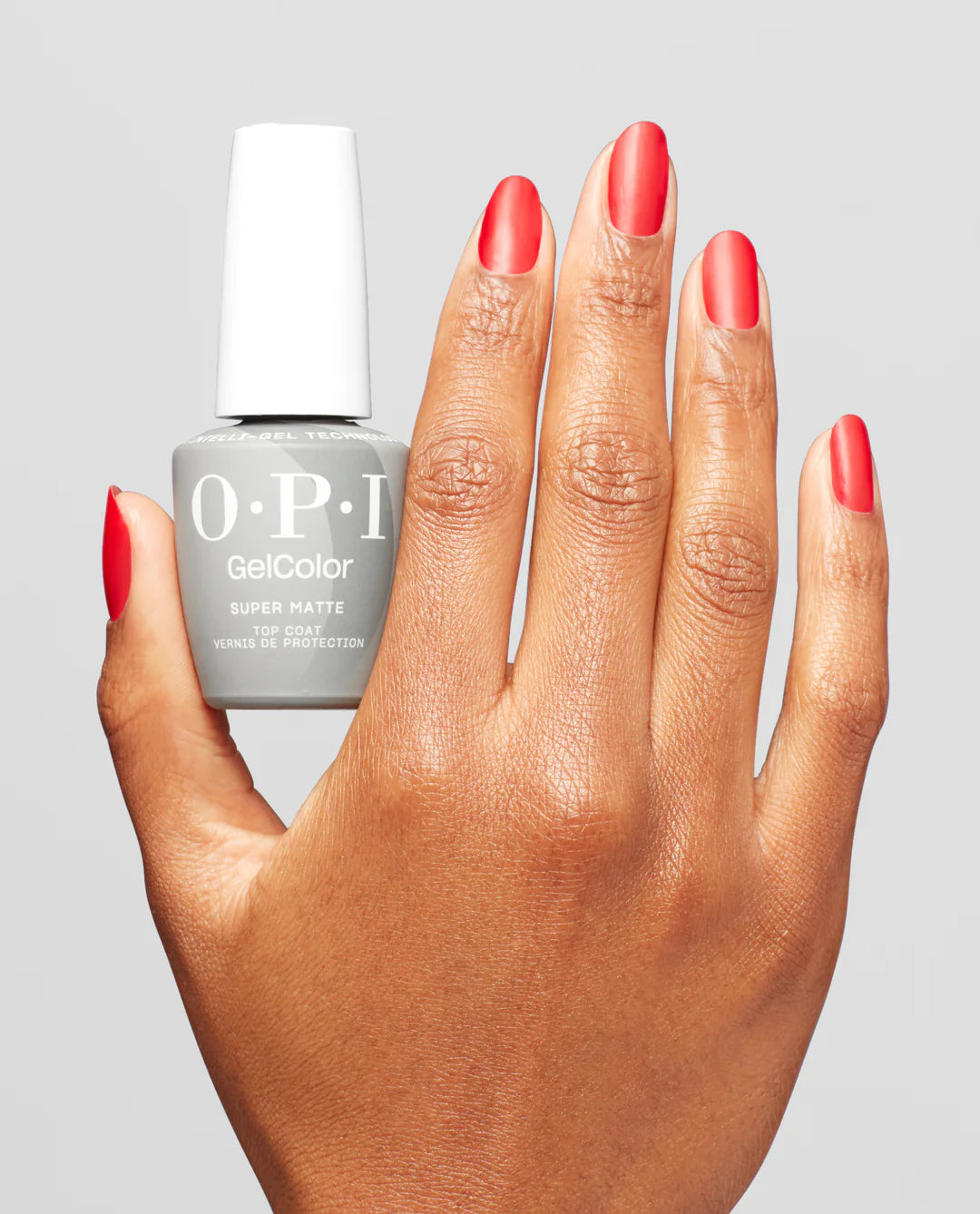 Hand with red nails holding an OPI GelColor Super Matte Top Coat GC004 on a gray background