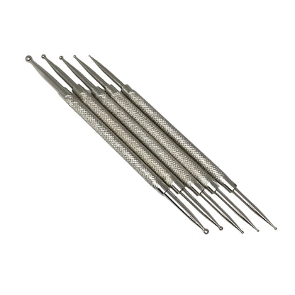 Six dotting tools for nail art with textured knurled handles and pointed tips, arranged diagonally on a plain white background.