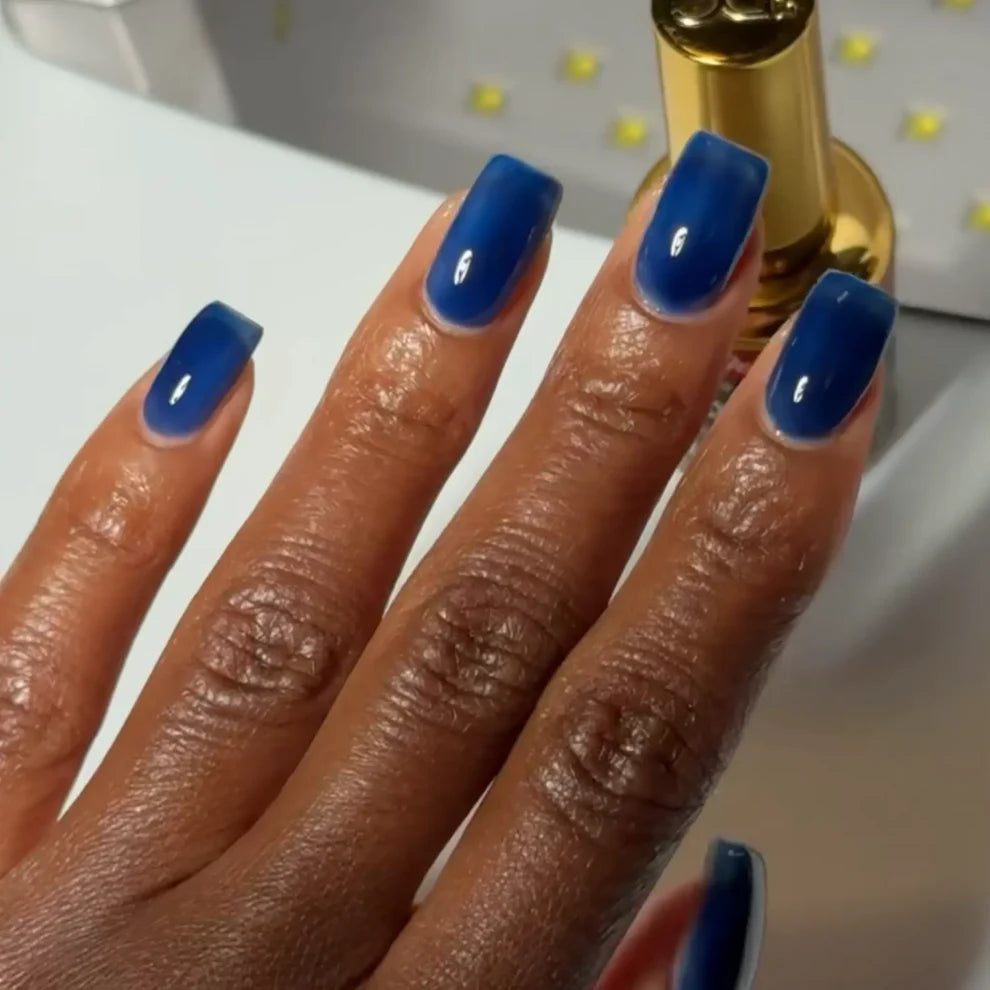 Manicured hand with dark skin tone wearing DC Jelly 021 Sapphire jelly gel polish in a deep teal blue finish