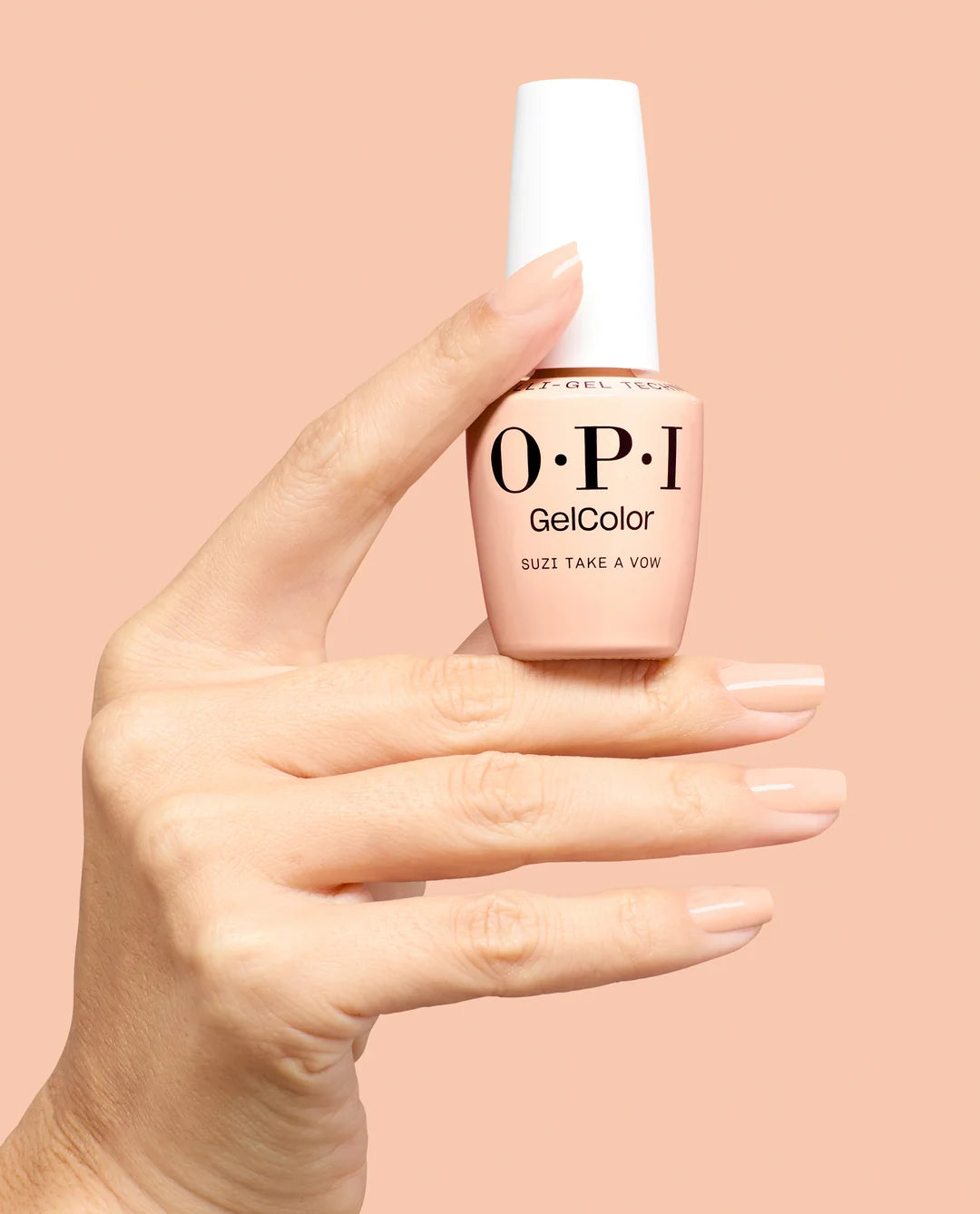 A hand holding an OPI GelColor nail polish bottle against a solid peach-pink background. The bottle contains a light peachy-pink polish and has a white cap.